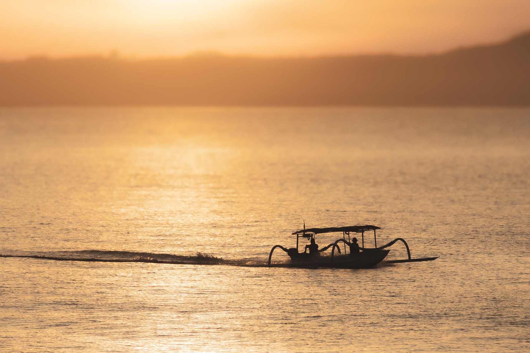 Traditional fishing boat silhouette crossing calm ocean waters during golden hour sunset. Warm sunlight reflects across the sea beneath a glowing pastel sky, creating a cinematic fine art seascape ideal for travel, coastal, and minimalist nature photography journal articles.