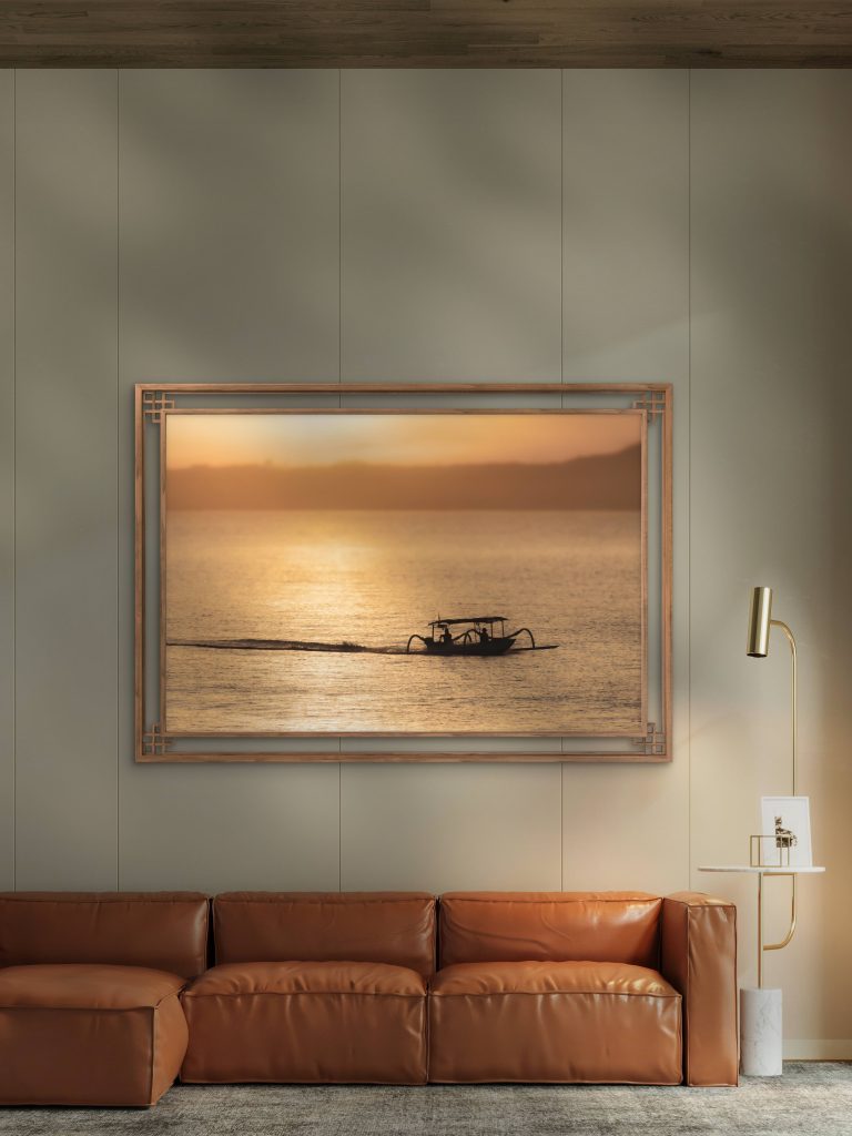 Framed fine art seascape photography displayed in a modern luxury living room interior. Minimalist wall art featuring a traditional fishing boat silhouette crossing calm golden ocean waters at sunset, styled with warm neutral tones for elegant contemporary home decor.