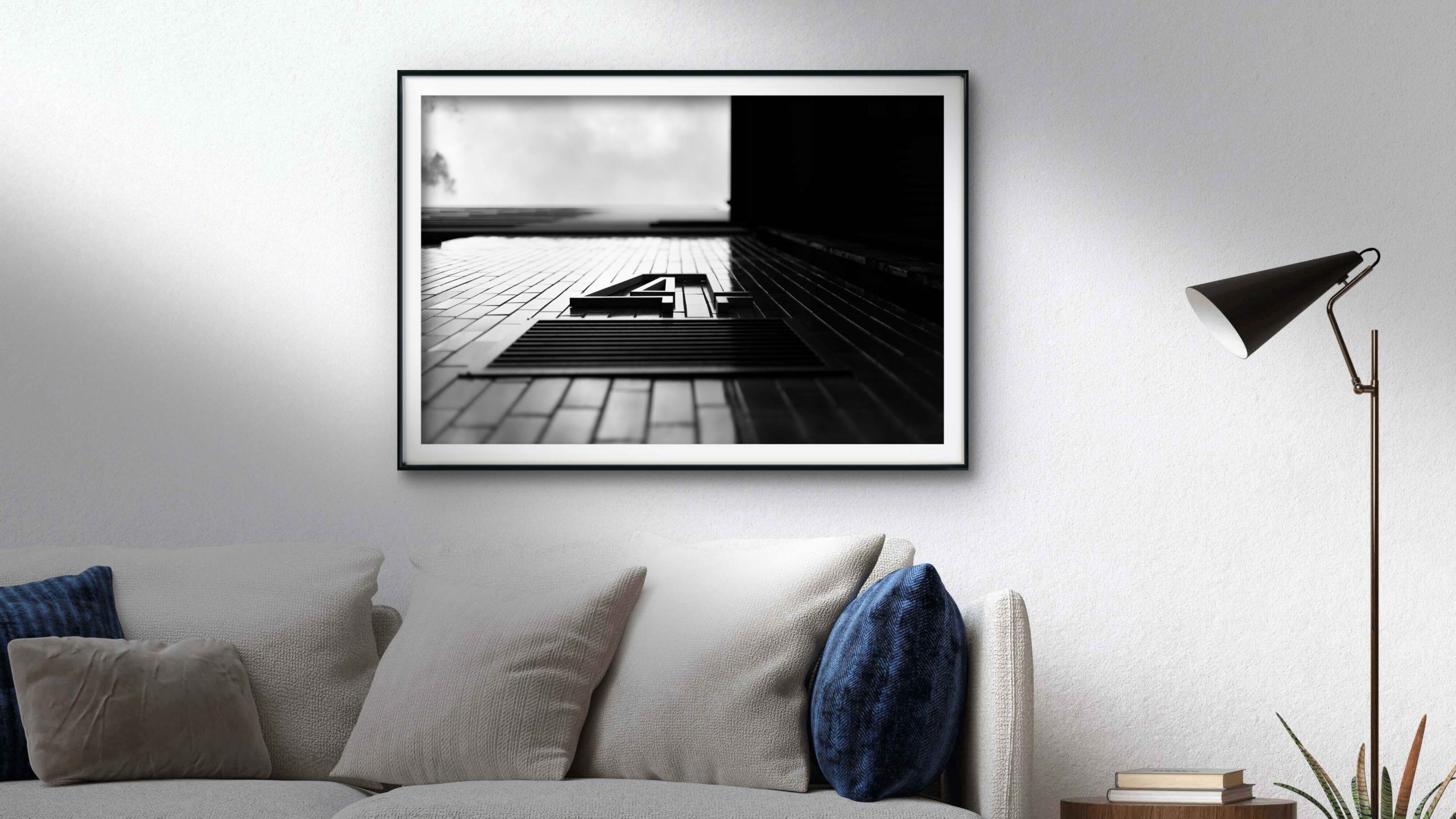 Minimal interior with a large framed black and white architectural print of a modern building seen from below, strong diagonals against a bright sky.