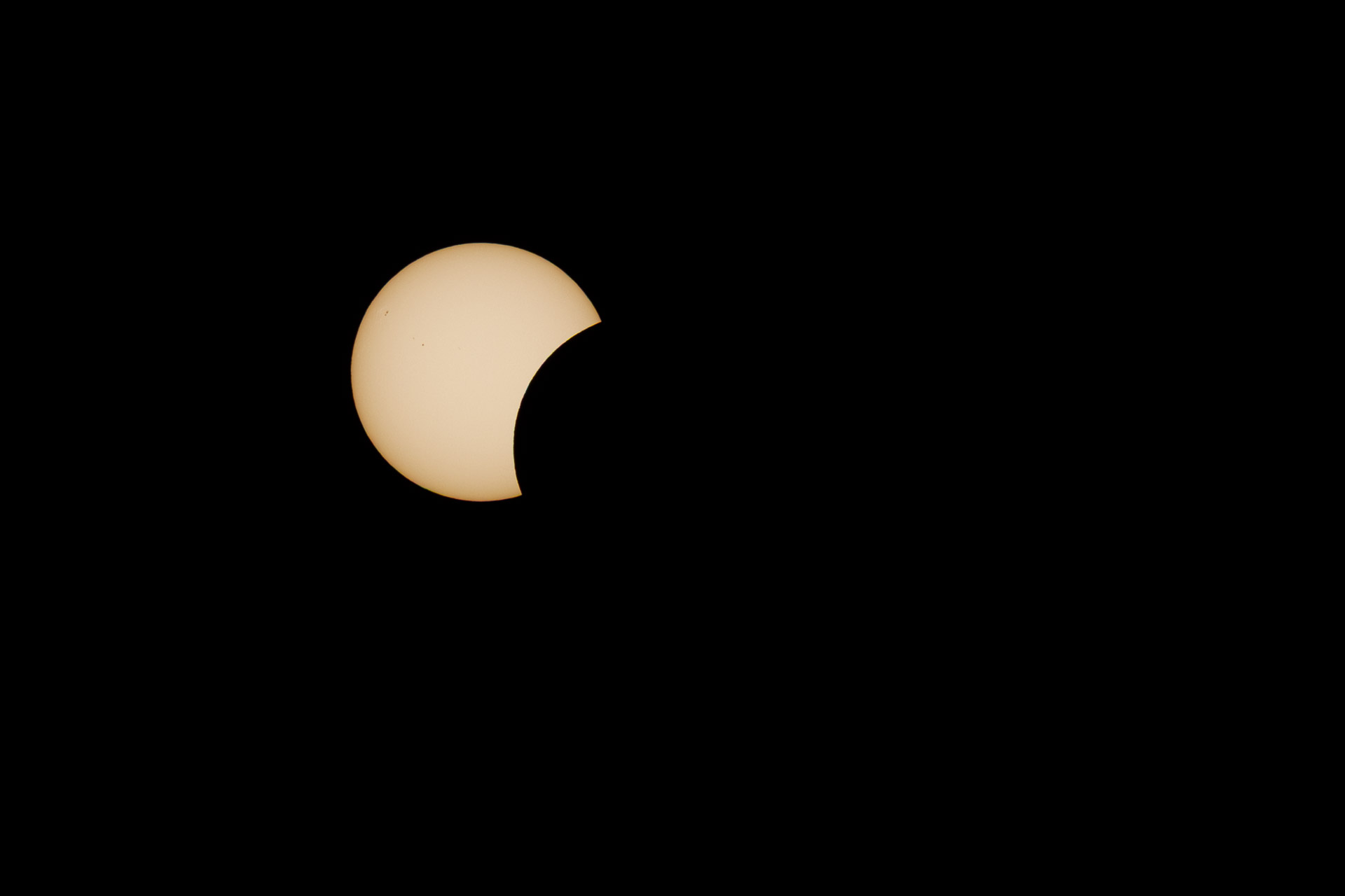 Pale solar disc against black, with a curved portion obscured at the lower right during a partial solar eclipse.